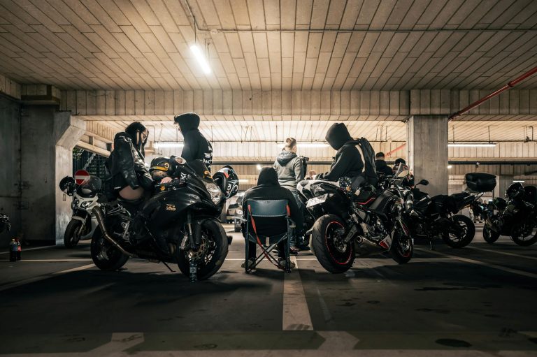 A group of people with motorcycles gather in an industrial parking garage, creating an urban subculture vibe. for Kutte Kulture LTD home